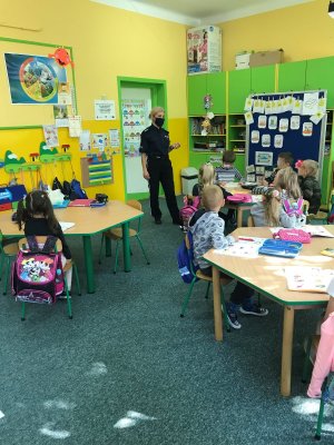 Policjantka stoi przed grupa przedszkolaków w sali lekcyjnej, które siedzą w ławkach