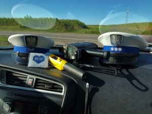 Dwie czapki policjantów z wydziału ruchu drogowego, leżące na desce rozdzielczej radiowozu wraz z miernikiem prędkości, urządzeniem do badania poziomu alkoholu w wydychanym powietrzu i ulotka.
