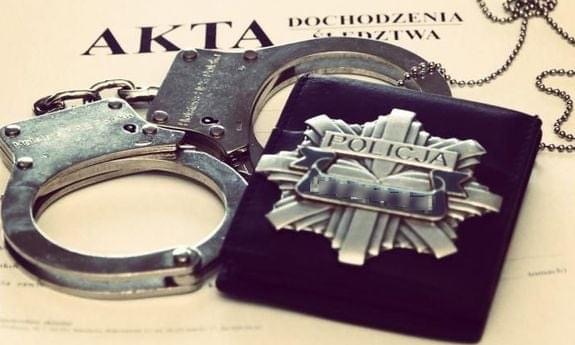 Kajdanki i policyjna odznaka, leżące na aktach dochodzenia/śledztwa.