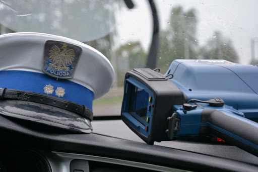 Czapka policjanta Wydziału Ruchu Drogowego i ręczny miernik prędkości, leżące na podszybiu radiowozu.