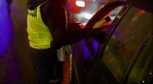 Noc. Policjant na drodze bada urządzeniem stan trzeźwości kierowcy, który siedzi wewnątrz pojazdu.
