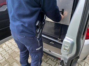 Policjant zamyka drzwi od przedziału dla osób zatrzymanych w pojeździe służbowym