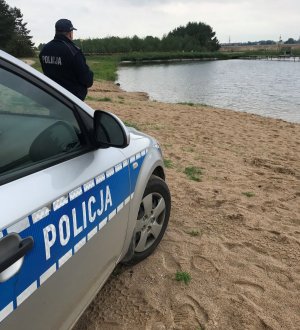 Radiowóz stojący na plaży, przy nim stoi policjant