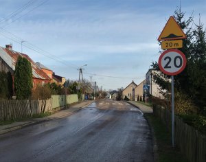 Ulica, przy której zamontowane są znaki ograniczające prędkość z informacja o progu zwalniającym. W oddali próg zwalniający.