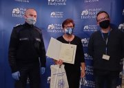 Na zdjęciu trzy osoby: policjant, seniorka, która trzyma dyplom i nagrodę, obok niej mężczyzna z Radia Białystok. W tle niebieski plakat z napisami: Polskie Radio Białystok.