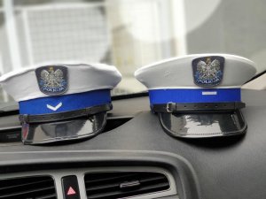Dwie czapki policjantów Wydziału Ruchu Drogowego leżące na desce rozdzielczej radiowozu.