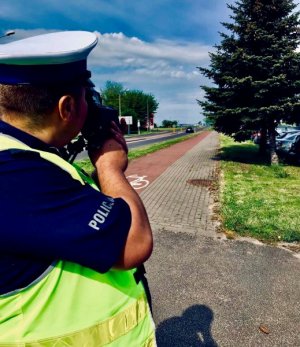 Umundurowany policjant przy drodze mierzy prędkość pojazdów ręcznym miernikiem prędkości.