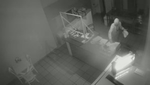 Zrzut ekranu z nagrania monitoringu. Na nim młody chłopak ubrany w białą bluzę za ladą w barze. Na głowie ma założony kaptur, a w dłoni chusteczki i plastikowy widelec.