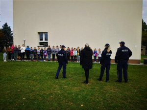 Teren przed szkołą. Dwie policjantki, policjant i kobieta, stoją przed grupą dzieci i młodzieży.