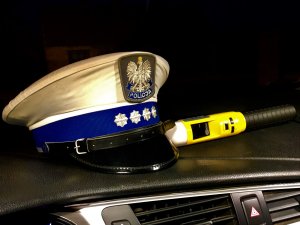 Noc. Czapka policjanta ruchu drogowego i urządzenie do badania stanu trzeźwości, leżące na podszybiu radiowozu.