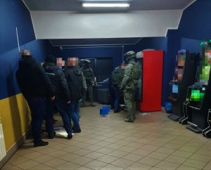 Funkcjonariusze KAS i nieumundurowani policjanci wewnątrz pomieszczenia, w którym stoją maszyny do gier hazardowych.
