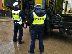 Dwóch policjantów na drodze przy samochodzie ciężarowym.