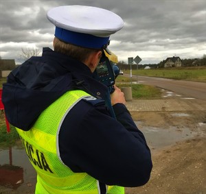 Policjant mierzy prędkość. Drogą jedzie samochód.