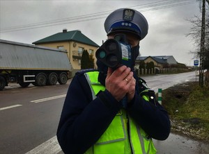 Policjant na drodze, przy pomocy urządzenia, mierzy prędkość pojazdów.