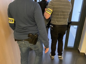 Dwóch policjantów wydziału kryminalnego prowadzi korytarzem zatrzymanego mężczyznę
