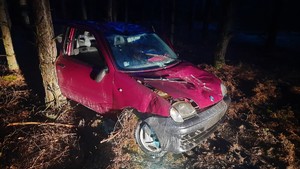Rozbity samochód osobowy w czerwonym kolorze w lesie.