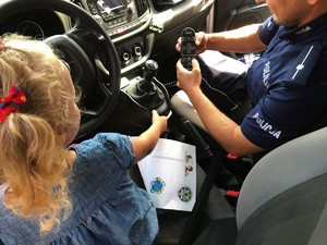Dzielnicowy w radiowozie z małą dziewczynką, która siedzi za kierownicą pojazdu