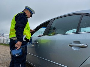 Policjant przeprowadza kontrolę drogową pojazdu osobowego w szarym kolorze