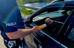 Policjant przy pomocy alkomatu przeprowadza badanie stanu trzeźwości kierowcy osobówki.