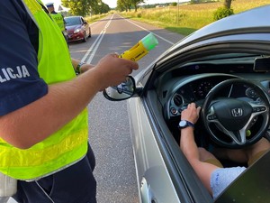 Policjant przy pomocy urządzenia bada stan trzeźwości kierowcy samochodu osobowego