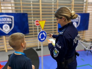 Policjantka z chłopcem na mobilnym miasteczku rozłożonym na sali gimnastycznej.