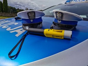 2 czapki policjantów ruchu drogowego i alkomat na masce policyjnego radiowozu