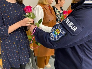 Policjant wręcza kobiecie różową różę