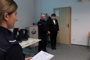 Na pierwszym planie policjantka. W oddali Komendant Powiatowy Policji w Kolnie stoi obok kobiety i przemawia.