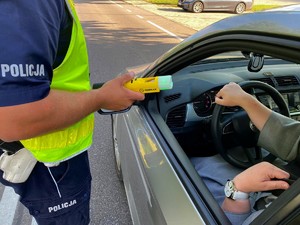 Policjant przy samochodzie osobowym za pomocą alkomatu kontroluje trzeźwość kierowcy.