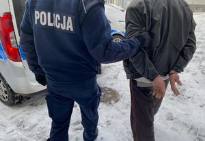 Policjant prowadzi mężczyznę, który ma założone kajdanki na ręce trzymane z tyłu