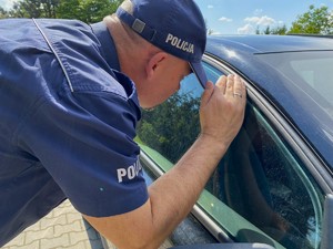 Świeci słońce. Policjant zagląda do wnętrza samochodu osobowego.