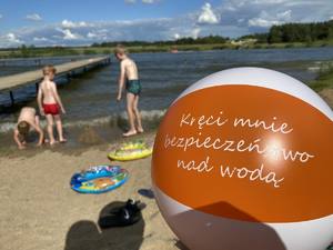 Piłka plażowa z napisem: Kręci mnie bezpieczeństwo nad wodą. W tle dzieci na plaży.