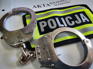 Kajdanki i opaska odblaskowa z napisem Policja na okładce akt dochodzenia/ śledztwa.