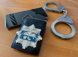 Telefon komórkowy, kajdanki i policyjna odznaka leżące na stoliku