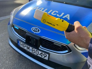 Policjant z alkomatem. W tle radiowóz