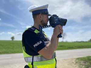 Policjant przy drodze za pomocą ręcznego miernika mierzy prędkość pojazdów