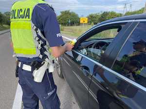 Policjant za pomocą alkomatu bada stan trzeźwości kierowcy osobówki