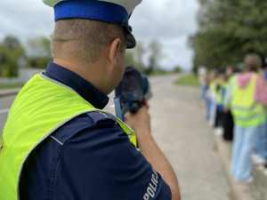 Policjant za pomocą ręcznego miernika mierzy prędkość pojazdów jadących drogą