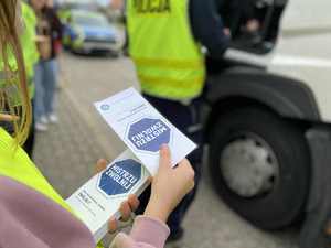 Policjant przeprowadza kontrole drogową. Dziecko trzyma ulotki informacyjne.