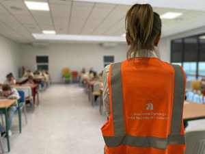 Kobieta w sali lekcyjnej. W ławkach siedzą dzieci