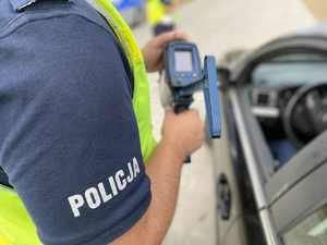 Policjant z ręcznym miernikiem prędkości przy samochodzie osobowym