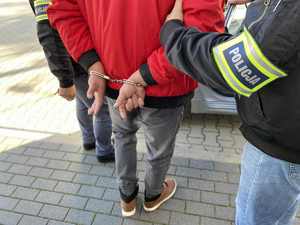 2 policjantów kryminalnych prowadzi zatrzymanego mężczyznę do radiowozu.