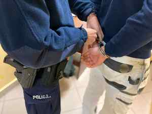 Policjant zakłada mężczyźnie kajdanki na ręce trzymane z tyłu