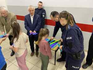 Policjanci i przedstawiciele lokalnego samorządu rozdają opaski odblaskowe dzieciom w szkole