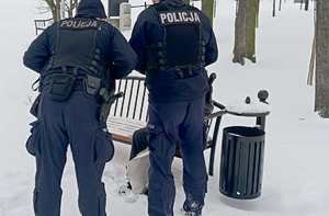 Wokół śnieg. Policjanci stoją przy ławce w parku, na której siedzi kobieta.