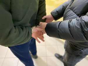 Nieumundurowany policjant zakłada zatrzymanemu mężczyźnie kajdanki na ręce trzymane z tyłu