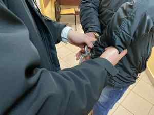 Nieumundurowany policjant zakłada zatrzymanemu mężczyźnie kajdanki na ręce trzymane z tyłu