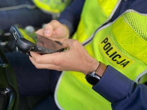Policjant siedzący w radiowozie trzyma w dłoniach terminal