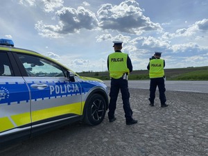 Policjanci stoją przy radiowozie przy drodze