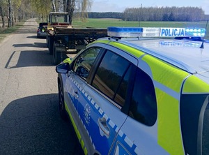 Radiowóz oraz ciągnik rolniczy z przyczepą na drodze.